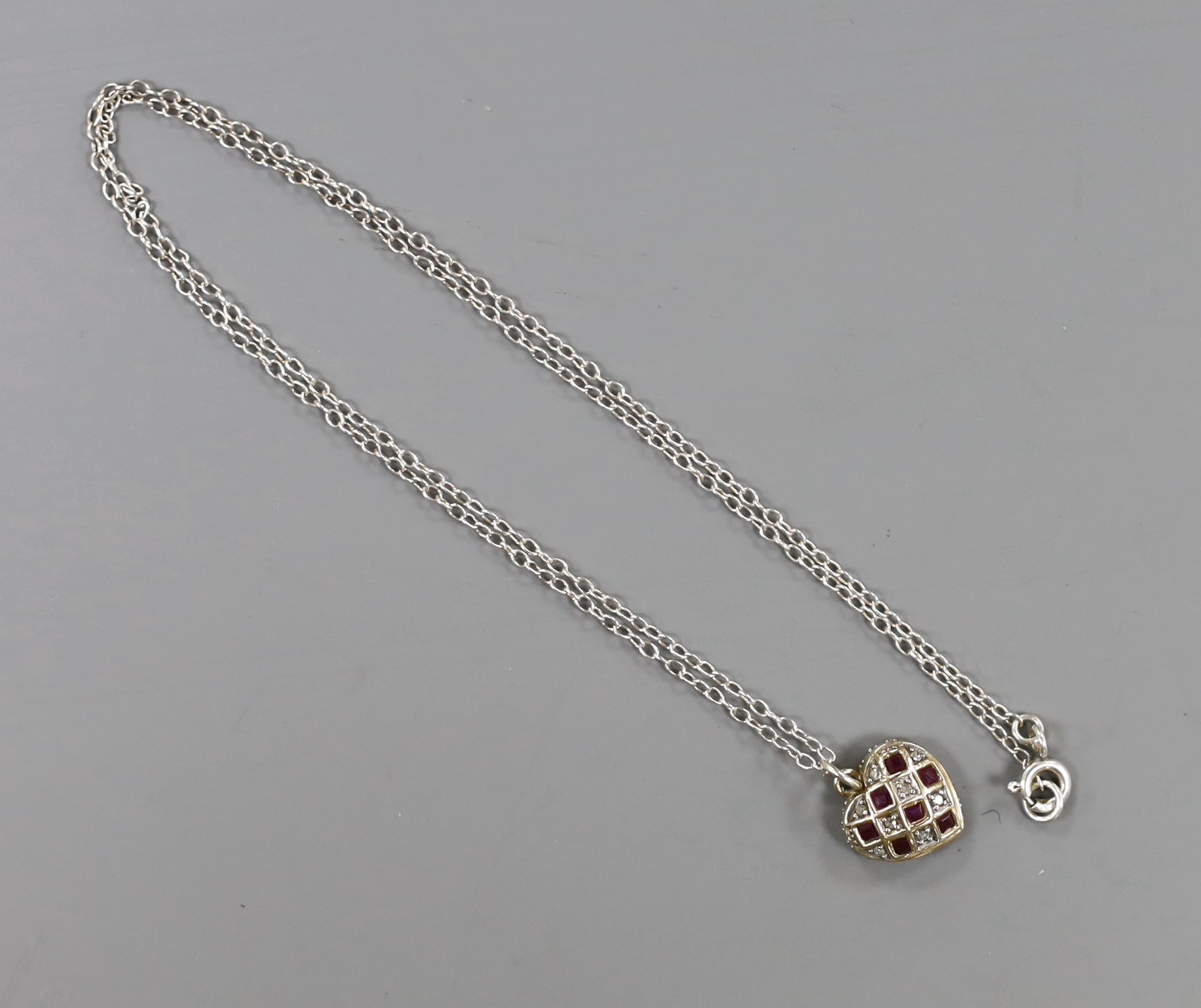 A modern yellow metal ruby and diamond set heart shaped pendant, 11mm,on a 925 chain.